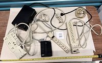 Photo showing all six power bars and surge protector units laid out on table with ruler for scale, cords tangled, items visibly used.
