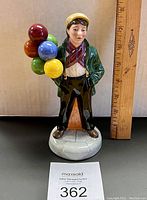 Front view of the Balloon Boy figurine with colorful balloons and a ruler for size reference.