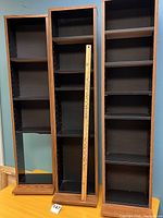 Front view of three tall shelving units with woodgrain exterior and black interior. Shows shelves and overall condition.