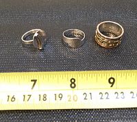 Six sterling silver rings on black fabric with a yellow measuring tape showing size markings in both inches and centimeters.