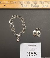 Sterling silver linked bracelet and pair of drop earrings with seller label and measuring ruler for scale.