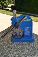 Front angle clear photo of blue arbor press showing handle, vertical ram, and cast iron base with slotted table.