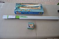 Guillow's Cessna Skyhawk balsa flying model kit box along with car trunk extender in front and long closet rod behind on table