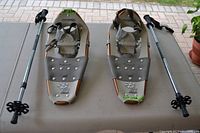 Top view of pair of Powderridge Crest snowshoes with adjustable hiking poles, showing bindings, metal crampons, and snow baskets on poles.