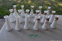 Front view of 17 white bud vases arranged on the grass, showing multiple with twine and red ribbon accents.