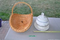 Wicker flower basket next to decorative ceramic soup tureen with lid and underplate on table outdoors