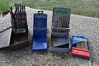 Four holders of drill bits displayed on table showing various sizes and metal/plastic indexes with LOT019 label.