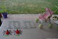 Photo of two metal ladybug garden ornaments, two chrome wine glass racks, and a pink doll carriage on a table with grass and patio bricks in background.