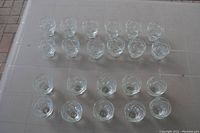 Top view of 22 clear glass candle holders in two groups on table: 10 larger holders and 12 smaller holders.