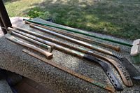 Hockey sticks alongside measuring tools and handles displayed on a textured surface outdoors with grass in background