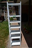 Full front view of tall white metal shelving unit with seven shelves outdoors, showing adjustable shelves and height.