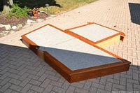 Three irregular-shaped wooden platform sections with grey carpeted tops set outdoors on a paved surface.