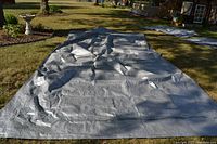 Gray nylon tarp laid out flat on grass showing surface and tie down rings