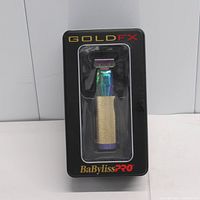 Front view of the BaByliss PRO Gold FX trimmer in retail packaging showcasing the trimmer with its gold knurled grip and multicolor head.