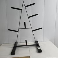 Front view of black metal A-frame weight plate rack with seven horizontal posts for storage, rubber feet visible on base.
