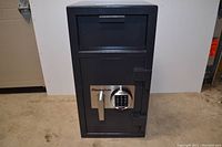 Front view of black SentrySafe depository safe showing closed door, digital keypad lock, lever handle and top deposit hopper