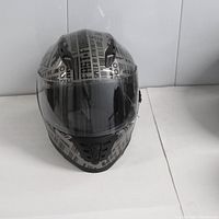 Front view of XL size motorcycle helmet showing black and gray graphic text design with clear visor and ventilation on chin area.