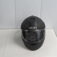 Front view of a matte black full-face motorcycle helmet showing the clear visor, ventilation vents, and HJC logo on forehead area.