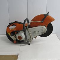 Left side view showing orange housing, white engine cover, front handle and blade guard