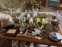 Wide shot of multiple items on a wooden table showing candle holders, corks, framed items, flowers, and various small collectibles.