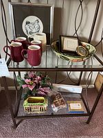 Top shelf display showing five purple pottery mugs and one cream mug in front of framed black and white art and a decorative bowl with frames.