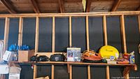 Wide shot of wooden shelf with assorted extension cords, booster cables, and hardware items arranged on it.