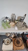 Wide view of the mid-century kitchen and serving items arranged on a table showing multiple glass sherbert dishes, metal cocktail shaker, cream-colored small dish, sifter, and the Juice-O-Matic juicer.