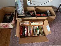 Four open boxes displaying contents: assorted train tracks, train cars mostly Tyco brand, some with packaging, and a control unit.