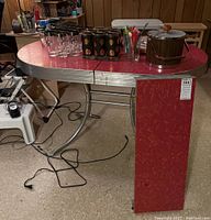 Full view of red Formica table with one drop leaf up, spare leaf panel leaning