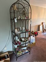 Front view of the ornate metal and glass arched shelf filled with various decorative items.