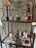 Full view of two glass shelves on a decorative metal frame holding various figurines, crystal pieces, a lamp, and candles.
