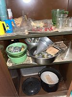 Shelf showing various vintage canning supplies including metal funnel, jars lids, jadeite bowls, glass beakers, and black metal pot with lid.
