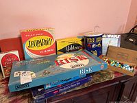 Photo showing vintage board games Jeopardy!, Yahtzee, Risk, Parker Brothers Continental Game, Space Age Stack-Ems toy, Star Wars item, and wooden box with marbles on a table.