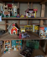 Four-shelf wooden shelving unit holding several vintage Fisher Price play toys and play sets. Visible are a castle, barn, McDonald's playset, small furniture pieces, figures, and containers.