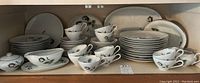 Wide view of the dishware set showing stacked dinner plates, tea cups, saucers, gravy dish, and serving bowls with floral patterns.