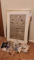 Framed display board with pins, loose baggies and piles of pins and patches on floor in front of board.