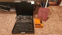 Vintage Smith Corona manual typewriter in open black carrying case with 9 typewriter ribbons box and 20th Century Typewriting lesson book placed on carpet.