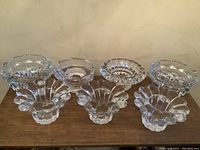 Front view of 10 clear crystal and glass votive candle holders arranged in two rows on a wooden surface showing different scalloped and geometric edge designs.
