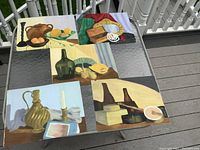 All five still life paintings arranged on a glass table outdoors showing the full lot and layout.