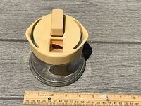 Top and side view of the vintage Aqua Blum flower stem cutter, showing glass container and beige lid with handle and cutting blade.