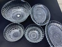 Set of five glass bowls arranged on a black surface including two oval dishes, two small round bowls, and one larger round bowl