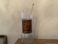 Full view of the 10 inch tall glass decanter featuring clear top and base with brown tinted middle section and metal stir rod inside.