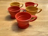 Top angle showing three orange and two yellow plastic cup holders with handles on a wooden surface.