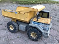 Photo of a large pressed steel Tonka dump truck in yellow and grey, with model number 354 visible, showing wear and rust, on a paved outdoor surface.