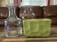 Photo of one green ceramic planter and two clear glass vases on a brown surface with ruler for scale.