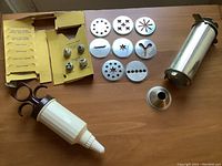 Two cookie press tools, eight decorative discs, and three nozzle tips laid out on table