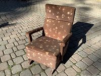Toddler rocking chair outdoors on stone patio, showing brown floral upholstery, wooden armrests, cushioned seat and backrest, and wooden base with springs.