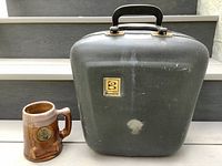 Front view of the pottery beer stein next to the Brunswick carrying case showing logo and handle.