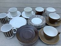 Another angle photo of the assortment of brown and white espresso cups, saucers, mugs and dishes showing the cracked mug and variety of dish patterns