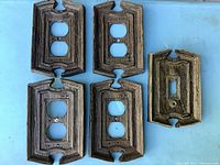 Photo of five vintage light switch and outlet cover plates, showing four duplex outlet covers and one single toggle switch cover plate all in textured brown plastic.
